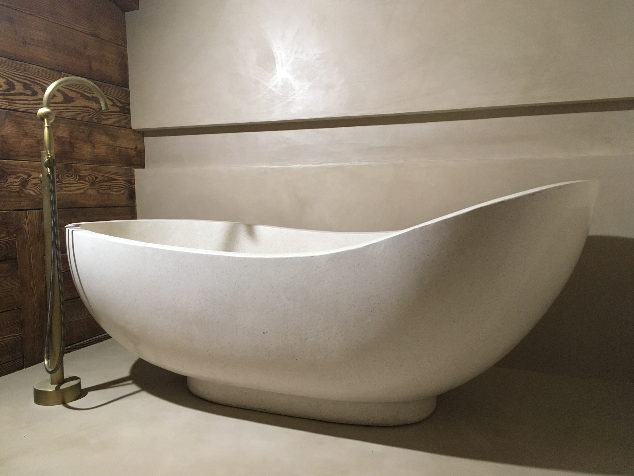 Réalisation Bio-Rénovation : baignoire îlot devant un mur décroché beige chaud, robinetterie sur pied en laiton