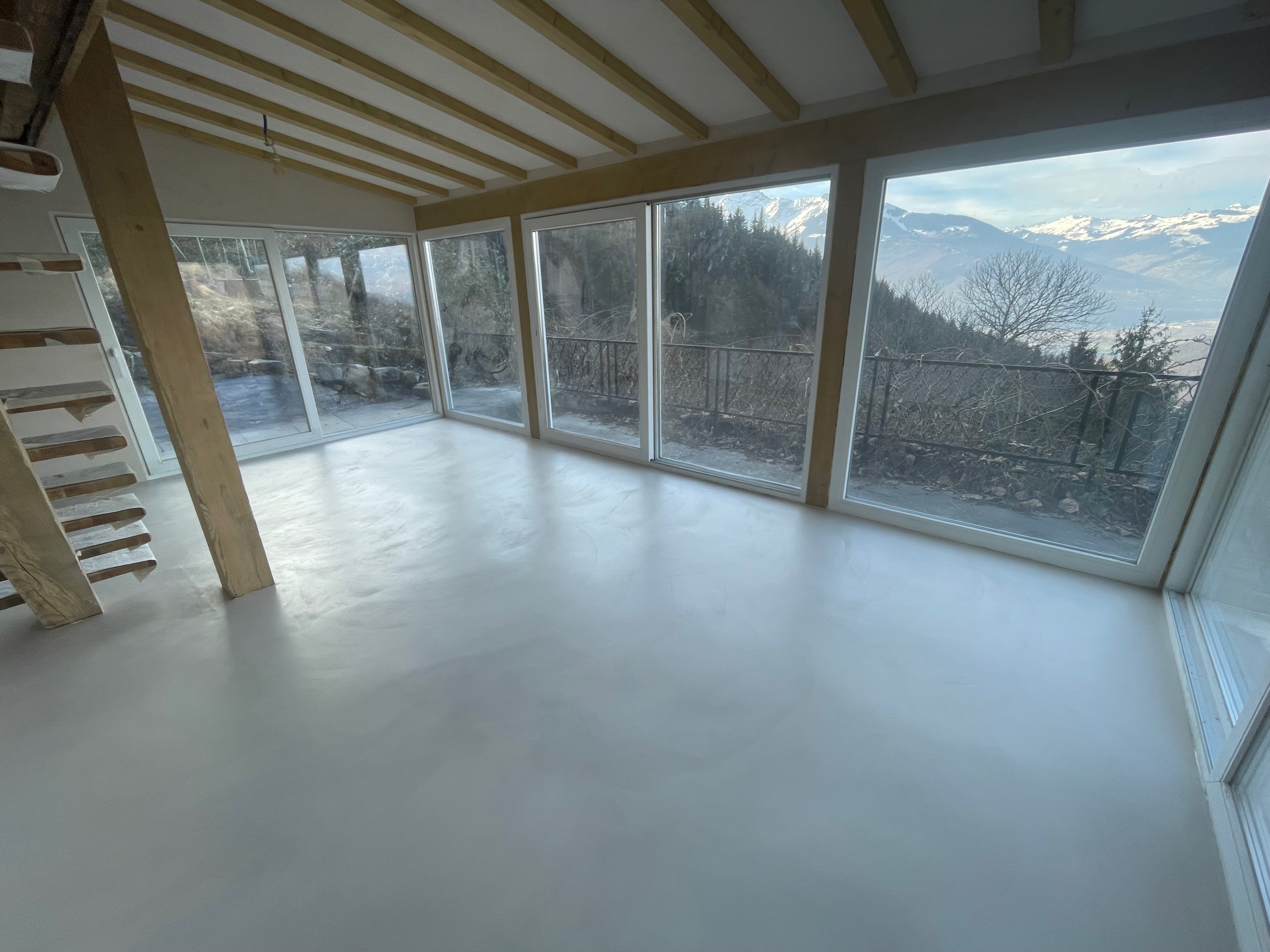 Réalisation Bio-Rénovation : sol continu en béton ciré clair en cours de finition, vue sur les Alpes